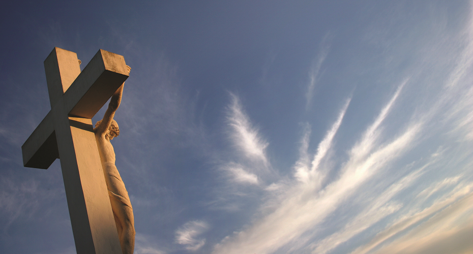 A statue of Christ on the cross against a blue sky with white clouds.