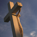 A statue of Christ on the cross against a blue sky with white clouds.