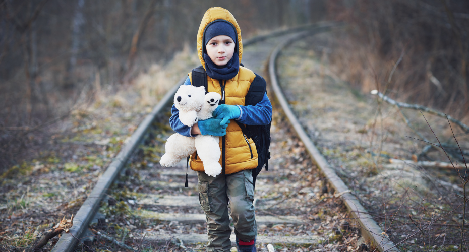 Child holding a teddy whilst walking along railway line.