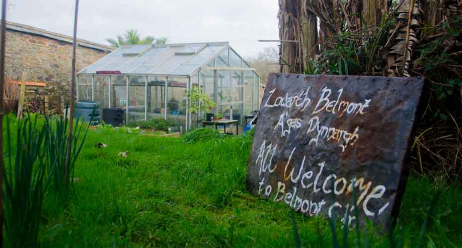 Greenhouse in background with handwritten sign in foreground saying All welcome to belmont gardens