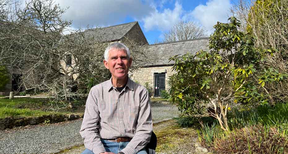 John Webb smiling into camera sat outside of chapel