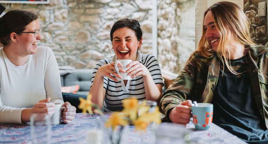 two female and one male student drinking tea around a table laughing