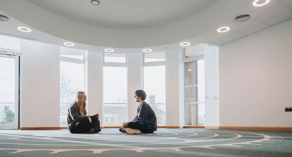 Students sitting crossed legged on the carpet in a prayer room.