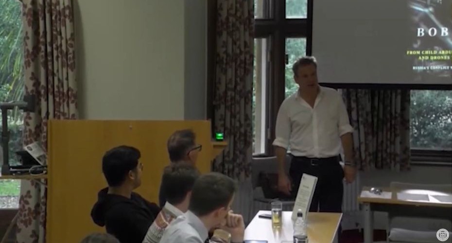 Dr Robert Seeley is stood in front of a large screen whilst delivering a lecture to a room of people.