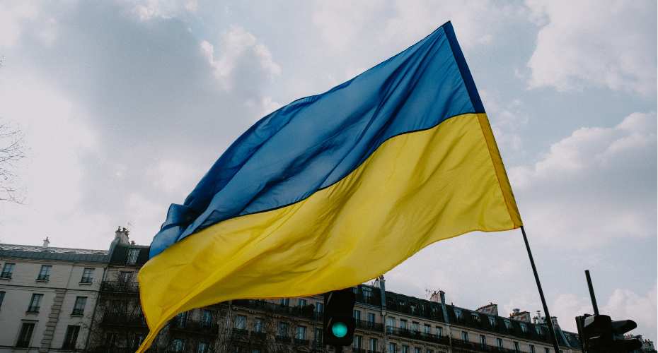 A blue and yellow flag of the Ukraine flapping in the wind in front of stone buildings
