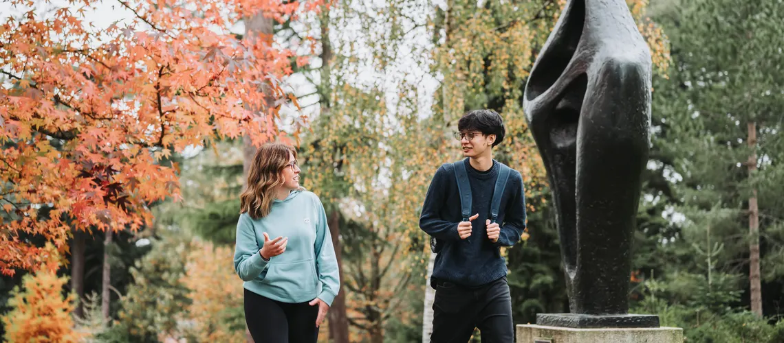 A pair of Humanities and Social Sciences students walking across Streatham Campus together in Autumn.