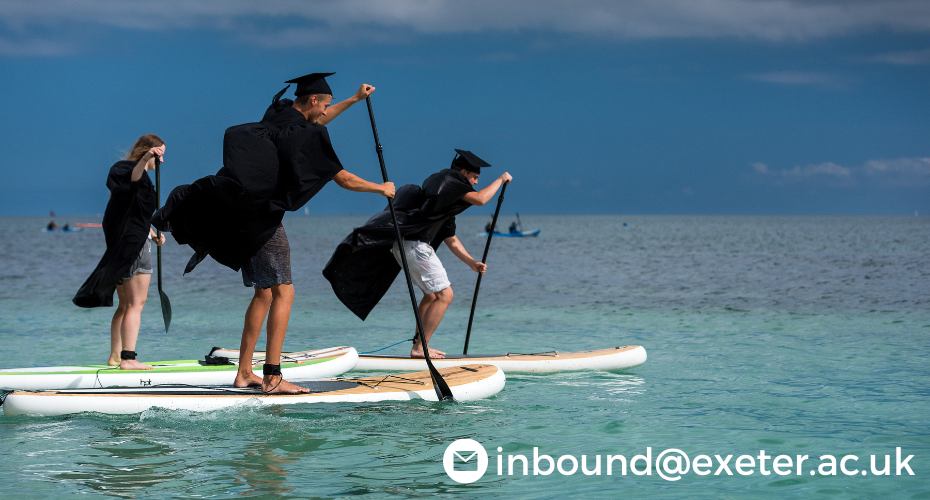 Graduates paddleboarding in gown and mortarboard