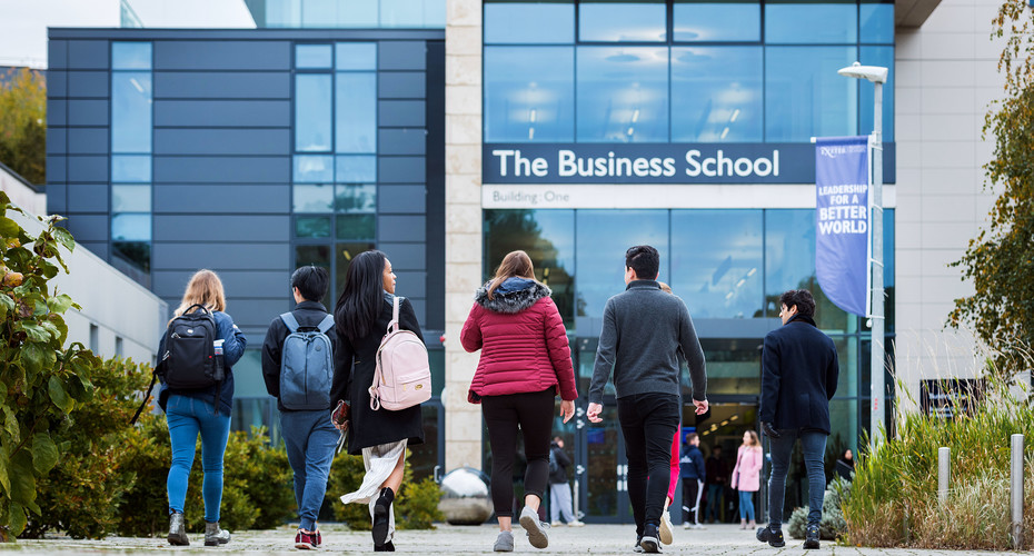 Students walk toward a large glass fronted building with the Business School written above the doorway