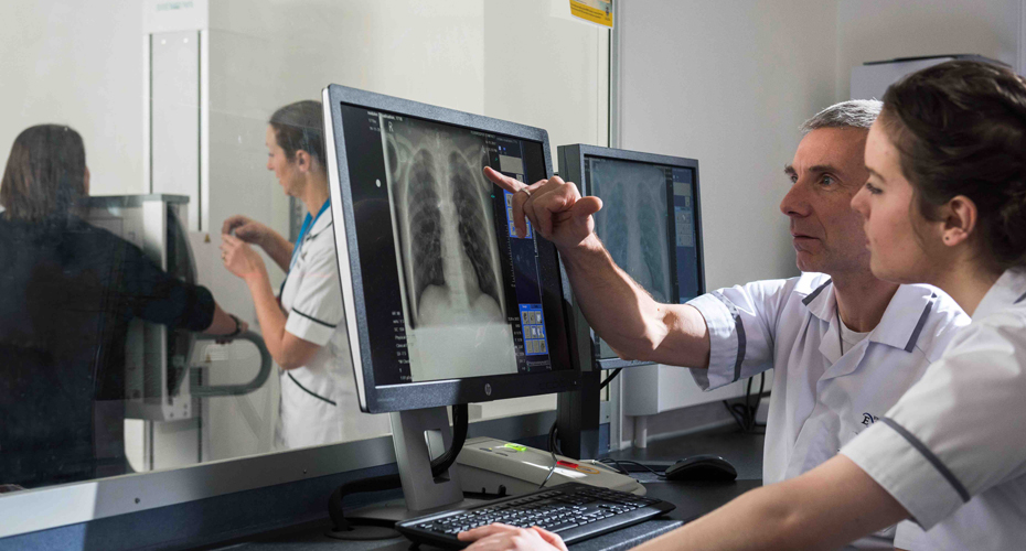 Two radiographers looking at a screen showing a chest x-ray