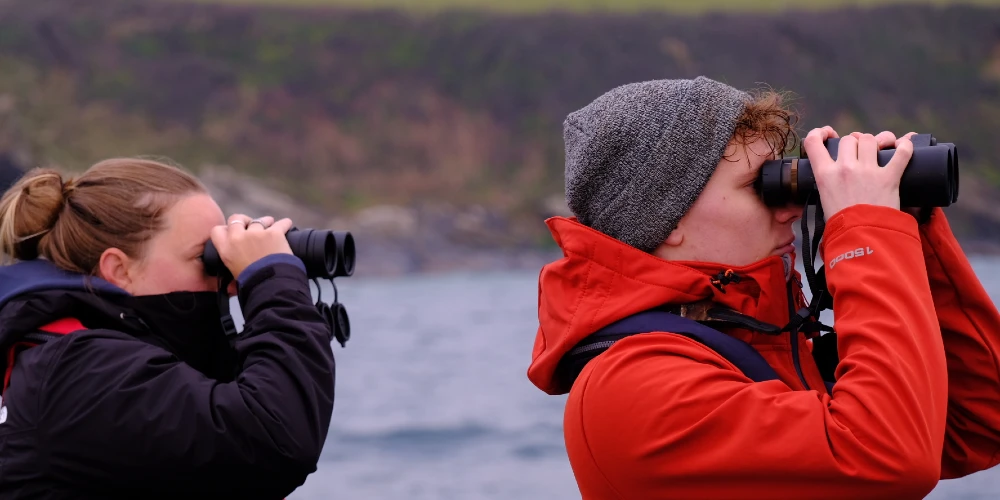 Picture of two people in a boat out at sea, each looking through binoculars
