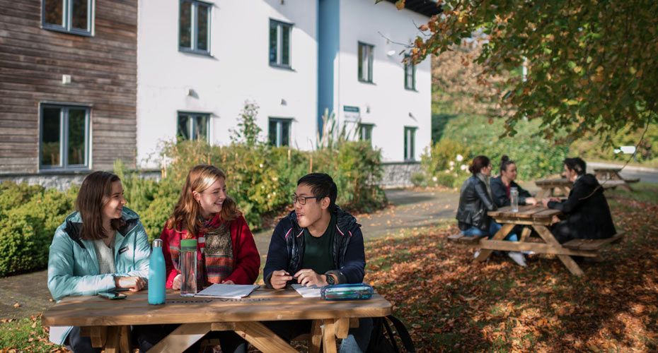 Students sitting at tables outside Glasney Student Village, studying and enjoying the crisp air and colorful foliage.