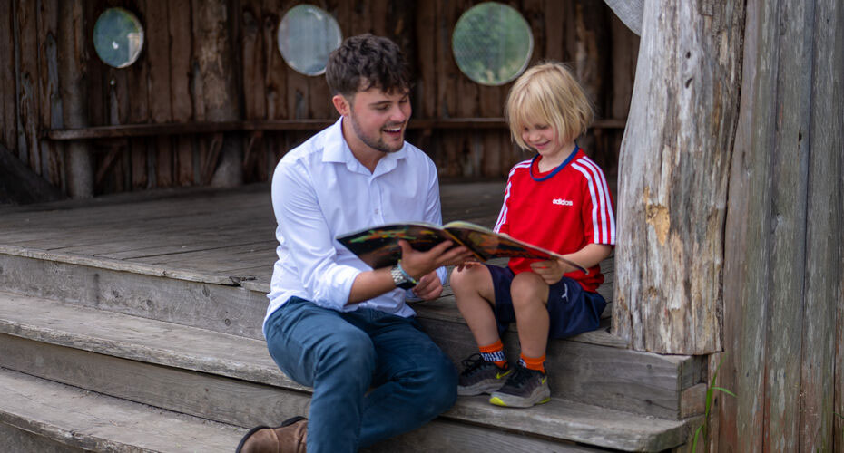 A man and child sitting on some steps with the child reading a book.