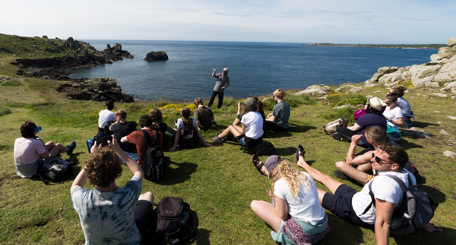 A lecturer teaching a group of students sitting by the coast on the Isles of Scilly