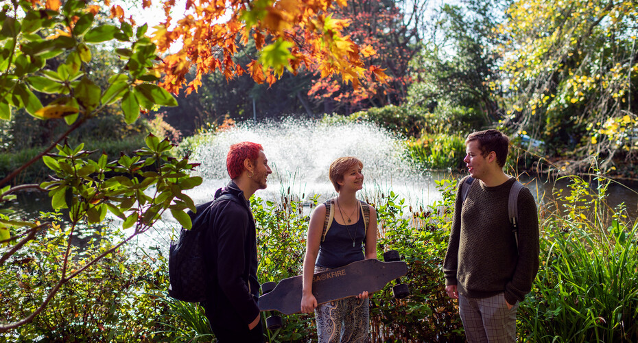 Three friends strolling by a pond in the grounds on Streatham Campus