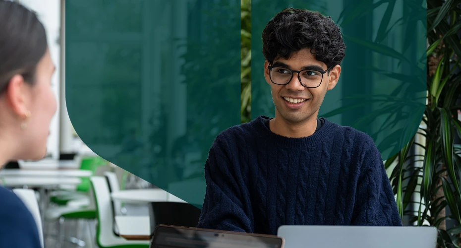 students sat at a table, in front of their laptops, laughing