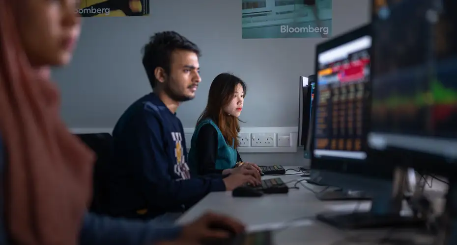 Students sitting at a long desk looking at a PC screen.