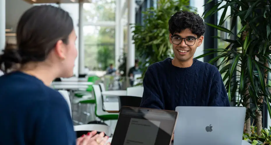 Sittings sitting around a table with laptops on and laughing.