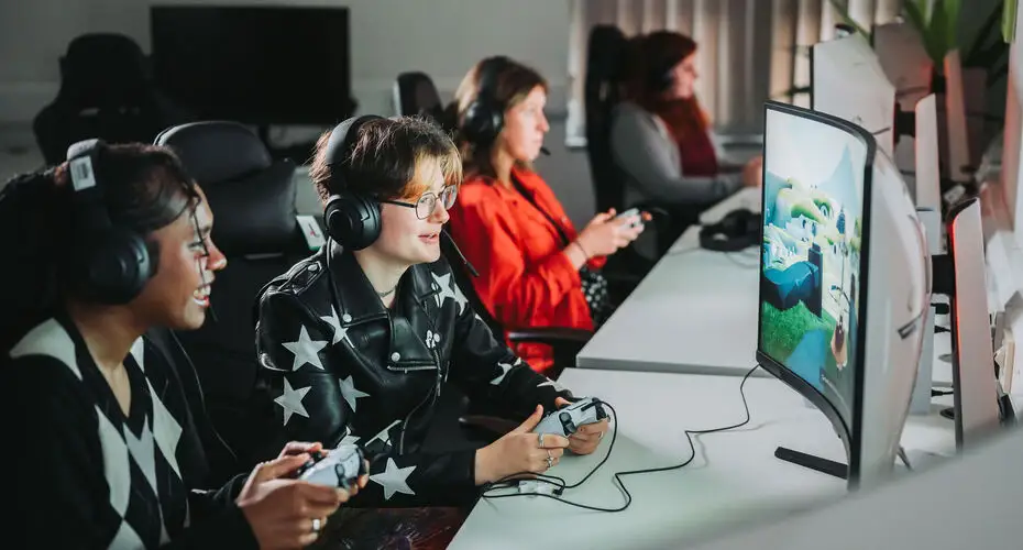 Students sitting in a line on a long desk with gaming controllers.
