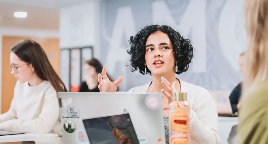 A lady sitting at a desk talking to students.
