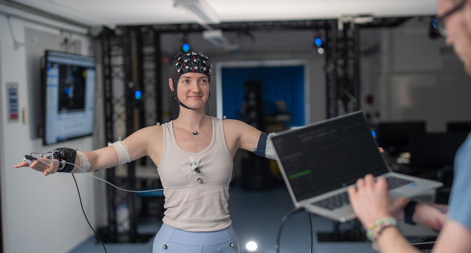 Person in a research lab with sensors on head and arms and another person typing into a laptop.