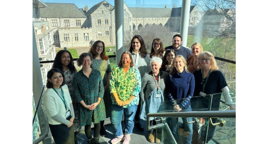 Picture of 13 people stood on a staircase in front of windows, with buildings and trees in the background