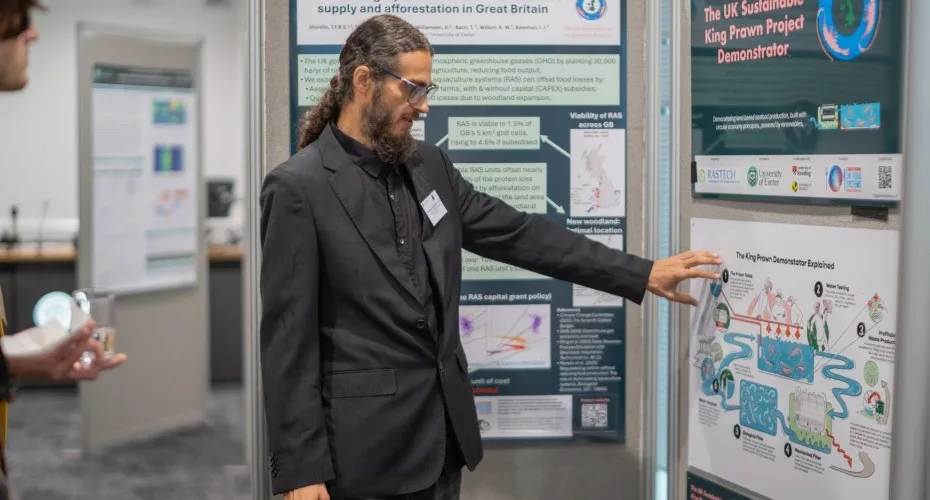 Thiago Morello presents his research poster at the LEEP@10 event, with attendees engaged in discussion nearby.