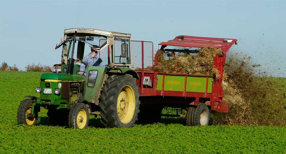 A tractor hauling a hay-filled trailer across a field.