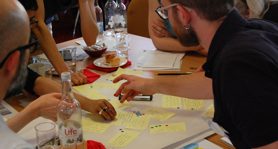 A diverse group of individuals sitting around a table covered in sticky notes, engaged in a discussion.