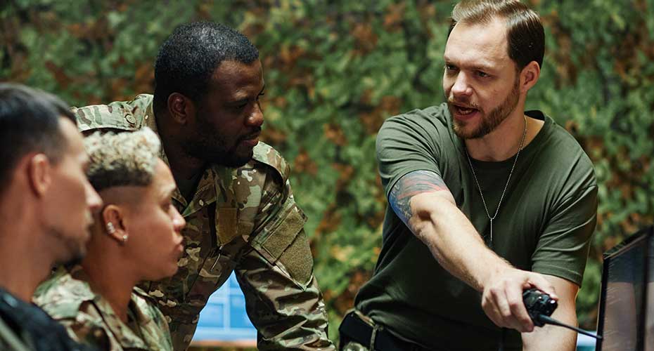 Young confident male officer with walkie-talkie in hand pointing forwards and speaking to group of intercultural colleagues at meeting