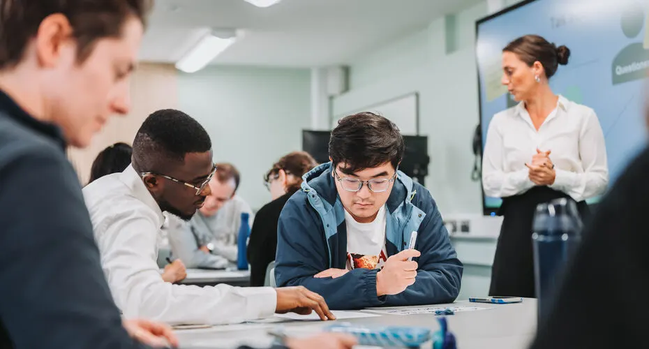 Group of maths students sitting around a desk working together, during a maths seminar
