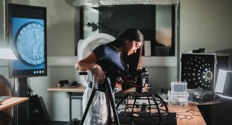 Student in a studio space using digital equipment to examine a historical coin.