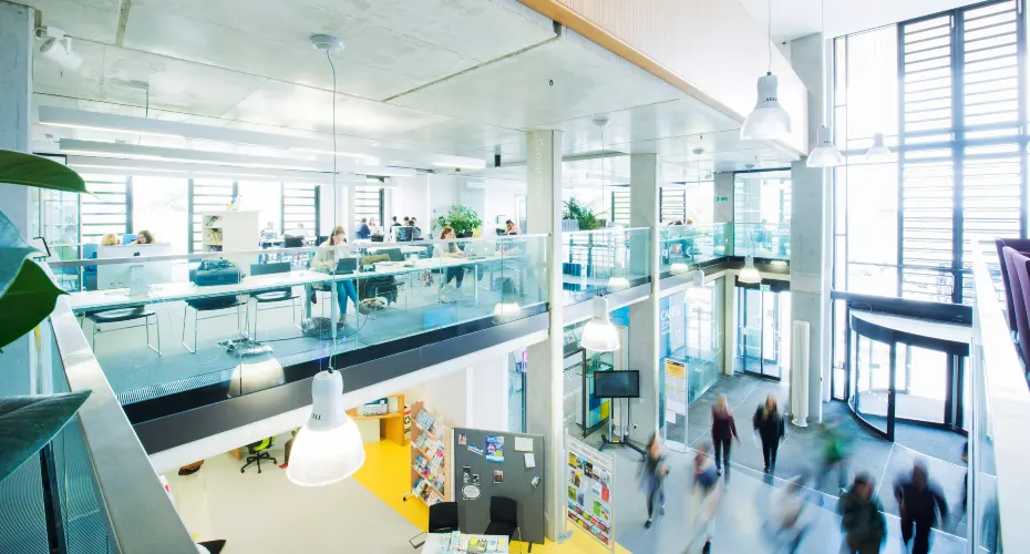 Image of inside a building on campus showing group study spaces, taken from the above, looking down from the upper floor.