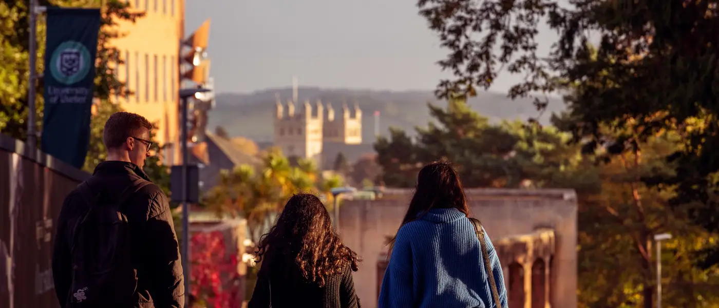 Three students walking down Queens drive at sunset with Exeter Catherdral in the distance.