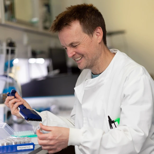 Professor Jonathan Mills wearing a lab coat and sitting at work bench.