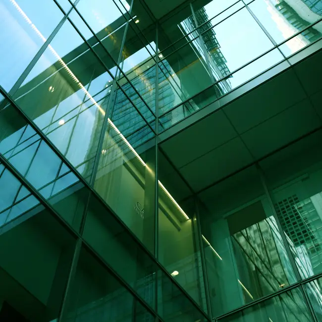 Glass windows of a tall building with the reflection of other windows in it.
