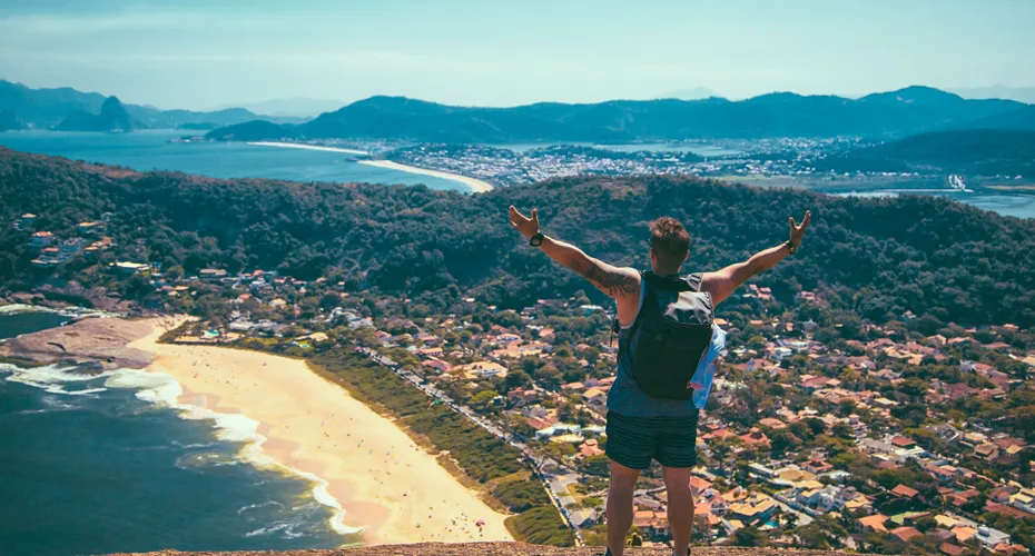 Individual on a mountain summit, arms lifted high in, surrounded by expansive views of nature.