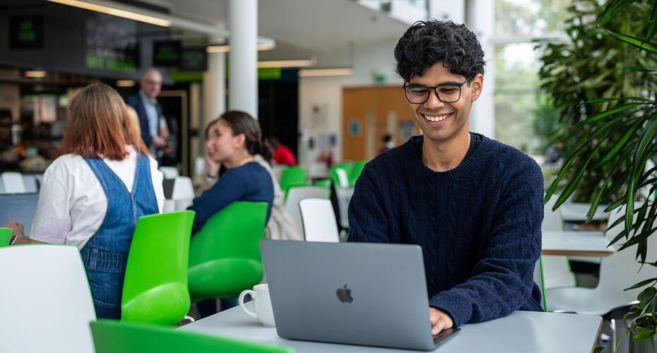 A student working on his laptop in a cafe on campus