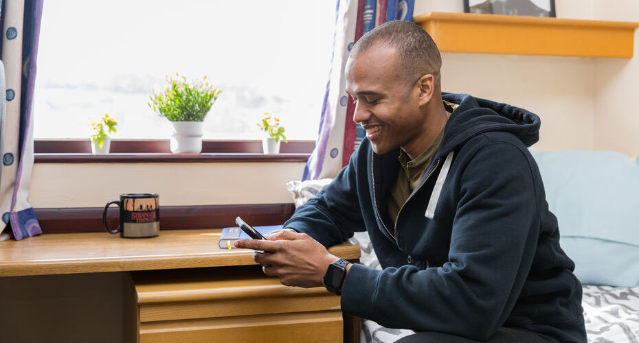 A student looking at his phone in his bedroom