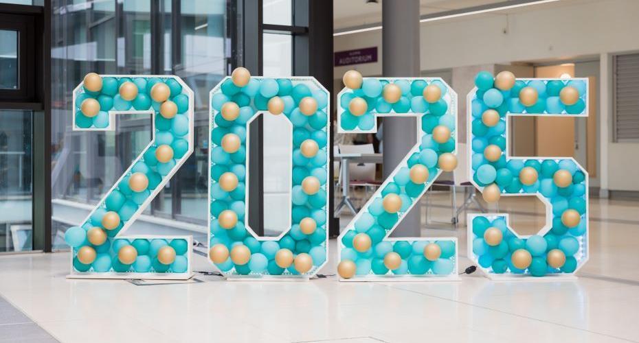 The number 2025, formed by four free-standing digits, each one about 2 meters tall and decorated with blue and gold balloons.