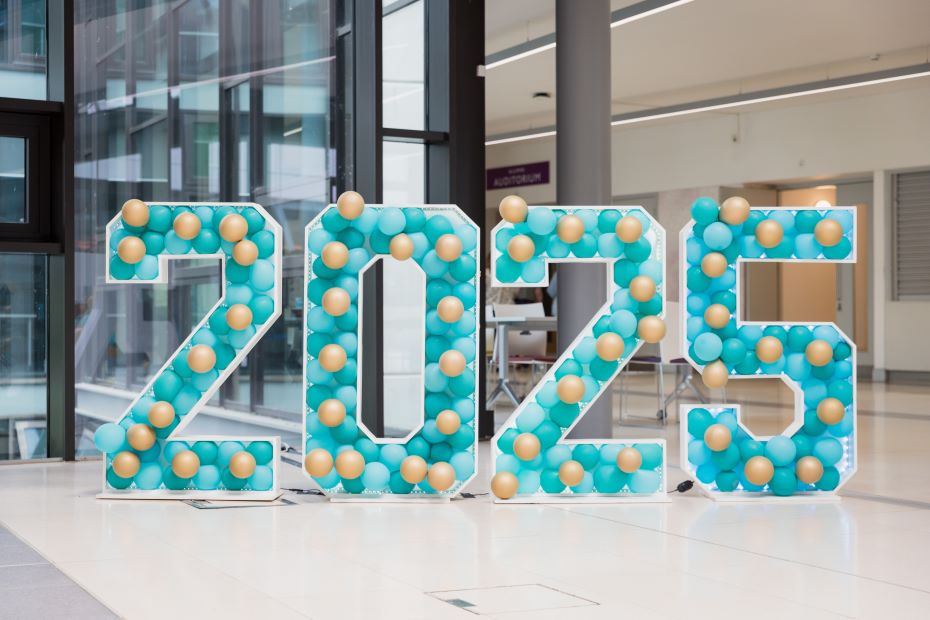 The number 2025, formed by four free-standing digits, each one about 7 feet high and decorated with blue and gold balloons.