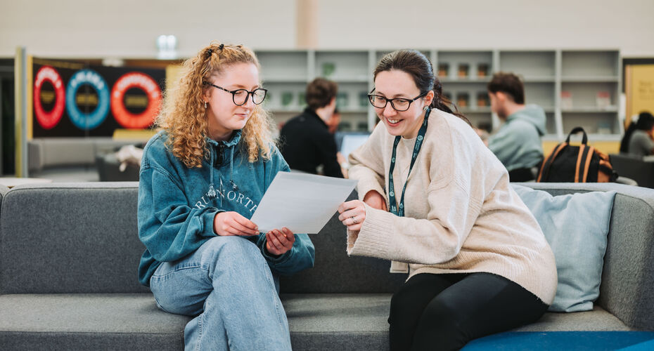 A student and member of careers staff are sat on a sofa in an open plan space, looking over the student's CV together