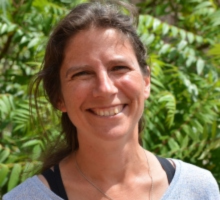 Photo of Elly Mosely, Anglican Chaplain, with lots of lush green leaves behind her