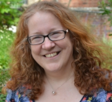 Photo of Jenny Hudson with green and buildings in the background. Jenny is wearing glasses and has ginger hair