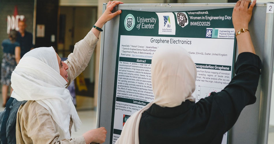 Two women wearing hijabs adjust a poster titled 
