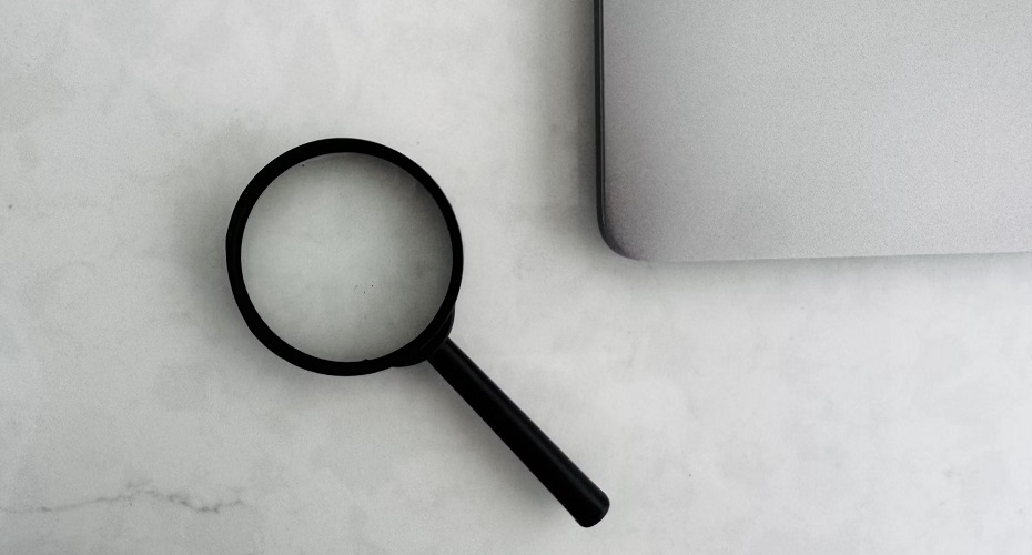 Magnifying glass beside the corner of a laptop on a marble surface