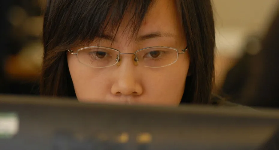 A person with glasses wearing a black shirt, looking directly at the camera with a neutral expression.