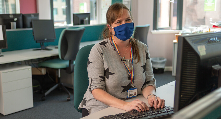 A staff member working at a computer, wearing a face mask