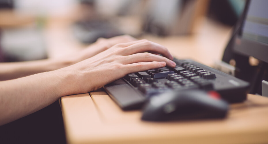 A student engaged in typing on a computer keyboard, surrounded by books and notes in a vibrant study area.